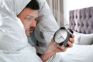 Sleepy man with alarm clock at home