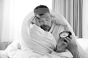 Sleepy man with alarm clock at home in morning. Black and white photography