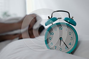Sleepy man awaking at home in morning, focus on alarm clock. Space for text