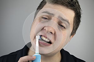 Sleepy man brushes his teeth with an electric brush. Oral hygiene concept. Tired man caring for teeth