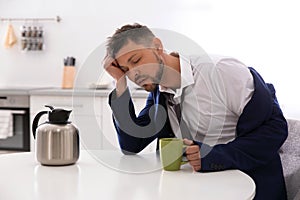 Sleepy man with cup of drink at home in morning