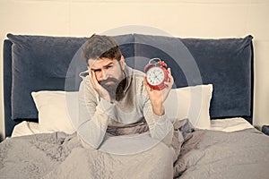 Sleepy man holding alarm clock being in bed in morning, time