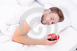 Sleepy man looking at alarm clock in hand while lying in bed. Morning awakening. Sleepy man turning off alarm clock