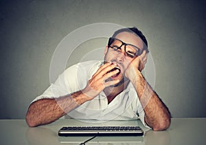 Sleepy man working on computer yawning