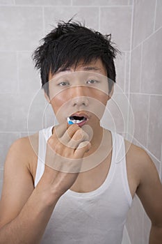 Sleepy mid adult man brushing teeth in bathroom