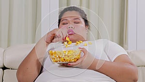 Sleepy obese woman eats popcorn on the couch