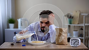 Sleepy overworked bachelor eating corn flakes with milk in morning, fatigue