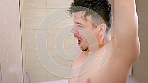 Sleepy shaggy young man stretches in front of bathroom mirror, yawns in morning.