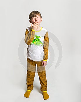 Sleepy and tired blond little cute boy wearing pajamas yawning. Kid boy in pyjamas with dinosaur animal print stands and
