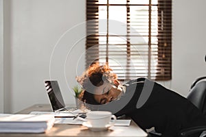 Sleepy and tired young black businesswoman or female office worker taking nap or sleep on her office desk