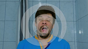 Sleepy tired young man is yawning at morning in bathroom looking at camera.