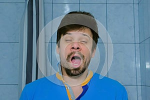 Sleepy tired young man is yawning at morning in bathroom looking at camera.