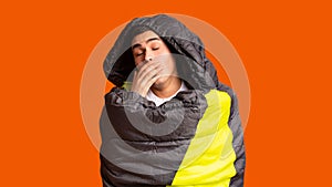 Sleepy tourist wrapped in sleeping bag, orange background