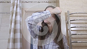Sleepy woken woman in glasses combs her hair in the bathroom.