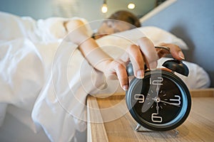 Sleepy woman in bed switching off alarm clock