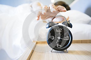 Sleepy woman in bed switching off alarm clock