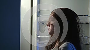 Sleepy woman grabs chocolate doughnut from fridge at night