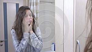 Sleepy woman with hangover in the bathroom looking at her reflection in the mirror.