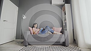 Sleepy woman lying on couch reading boring book at home. College girl student study in sofa looking textbook feel bored