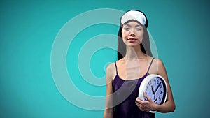 Sleepy woman in pajamas holding clock, importance of sleep schedule for health