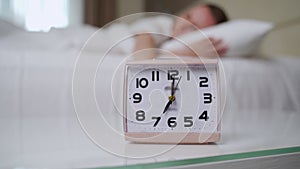 Sleepy woman reaches hand to turn off ringing alarm clock