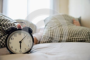 Sleepy woman reaching holding the alarm clock in the morning with late wake up