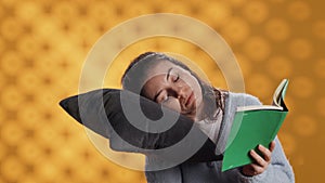 Sleepy woman struggling to keep eyes open while reading book, studio background