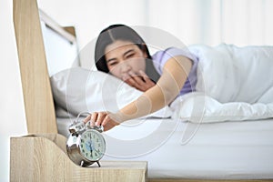 Sleepy woman waking up to turn off the alarm clock while still yawning in bed