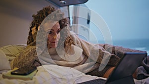 Sleepy woman watching film at laptop lying campervan bed at evening close up.