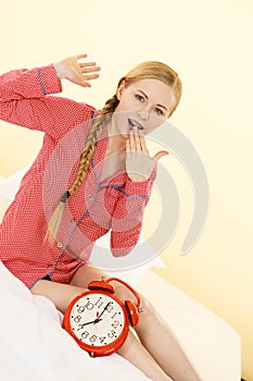 Sleepy woman wearing pajamas holding clock