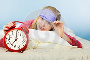 Sleepy woman wearing pajamas holding clock