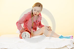 Sleepy woman wearing pajamas holding clock