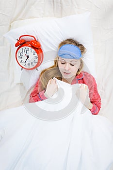 Sleepy woman wearing pajamas holding clock