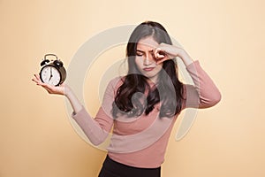 Sleepy young Asian woman with a clock in the morning.