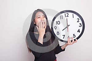 Sleepy young Asian woman with a clock in the morning.