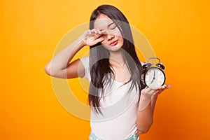 Sleepy young Asian woman with a clock in the morning.