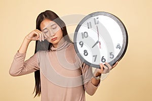 Sleepy young Asian woman with a clock in the morning