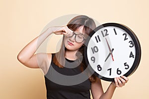 Sleepy young Asian woman with a clock in the morning