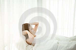 Sleepy young asian woman stretching and waking up in her bedroom at home in the morning