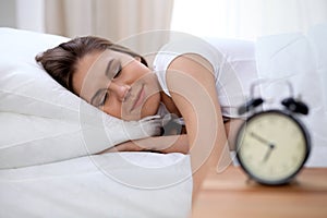 Sleepy young brunette woman stretching hand to ringing alarm willing turn it off. Early wake up, not getting enough