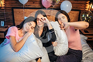 Sleepy young models sit together on bed in festive room. They want to sleep. One of them is already sleeping.