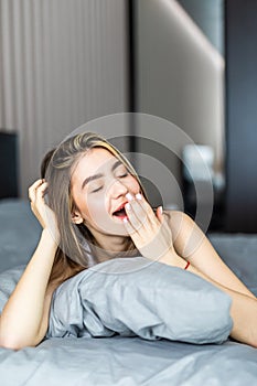 Sleepy young pretty woman yawning in bed at home