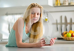 Sleepy young woman with cup of coffee in kitchen