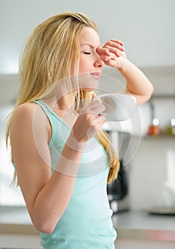 Sleepy young woman with cup of coffee in kitchen