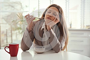 Sleepy young woman eating breakfast at home in morning