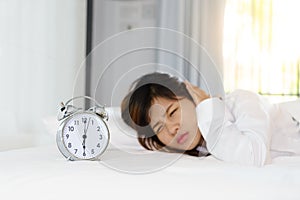 Sleepy young woman looking at alarm clock with hands covering he