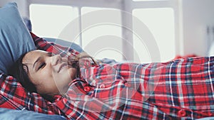 Sleepy young woman in pajamas lying in bed waking up stretching and smiling in the morning