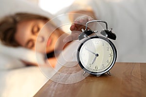 Sleepy young woman stretching hand to ringing alarm willing turn it off. Early wake up, not getting enough sleep