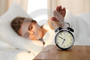 Sleepy young woman stretching hand to ringing alarm willing turn it off. Early wake up, not getting enough sleep