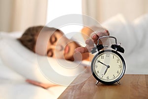 Sleepy young woman stretching hand to ringing alarm willing turn it off. Early wake up, not getting enough sleep